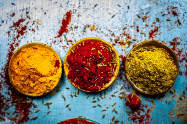 Close up of three basic,main and essential ingredients or spices of Indian/Asian food on a silver wooden surface i.e. Coriander powder,turmeric powder and the spicy Red chili powder.